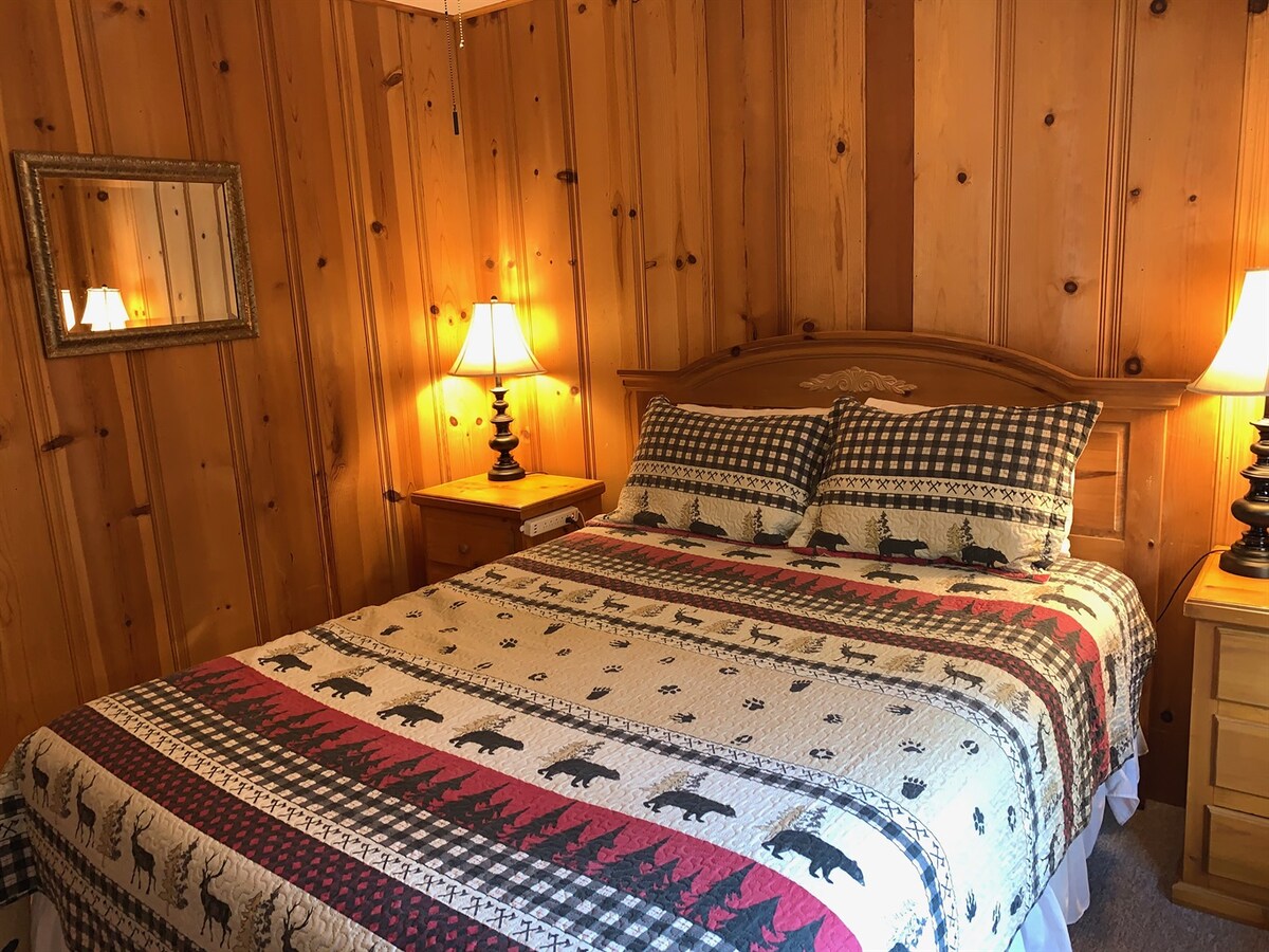 Middle bedroom with queen bed and warm wood paneling.